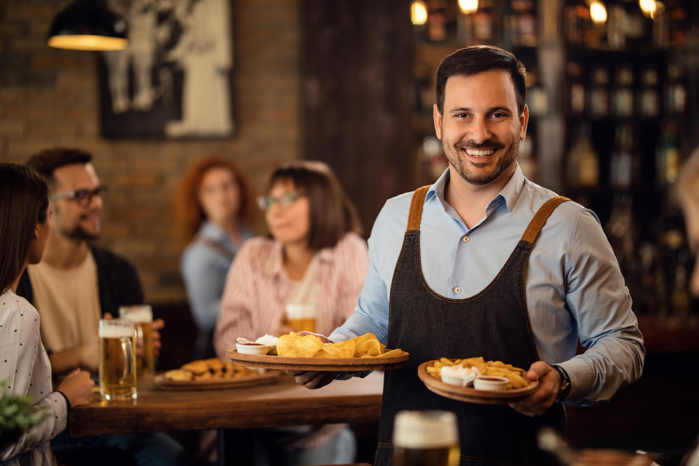happy-waiter-holding-plates-with-food-looking-camera-while-serving-guests-restaurant