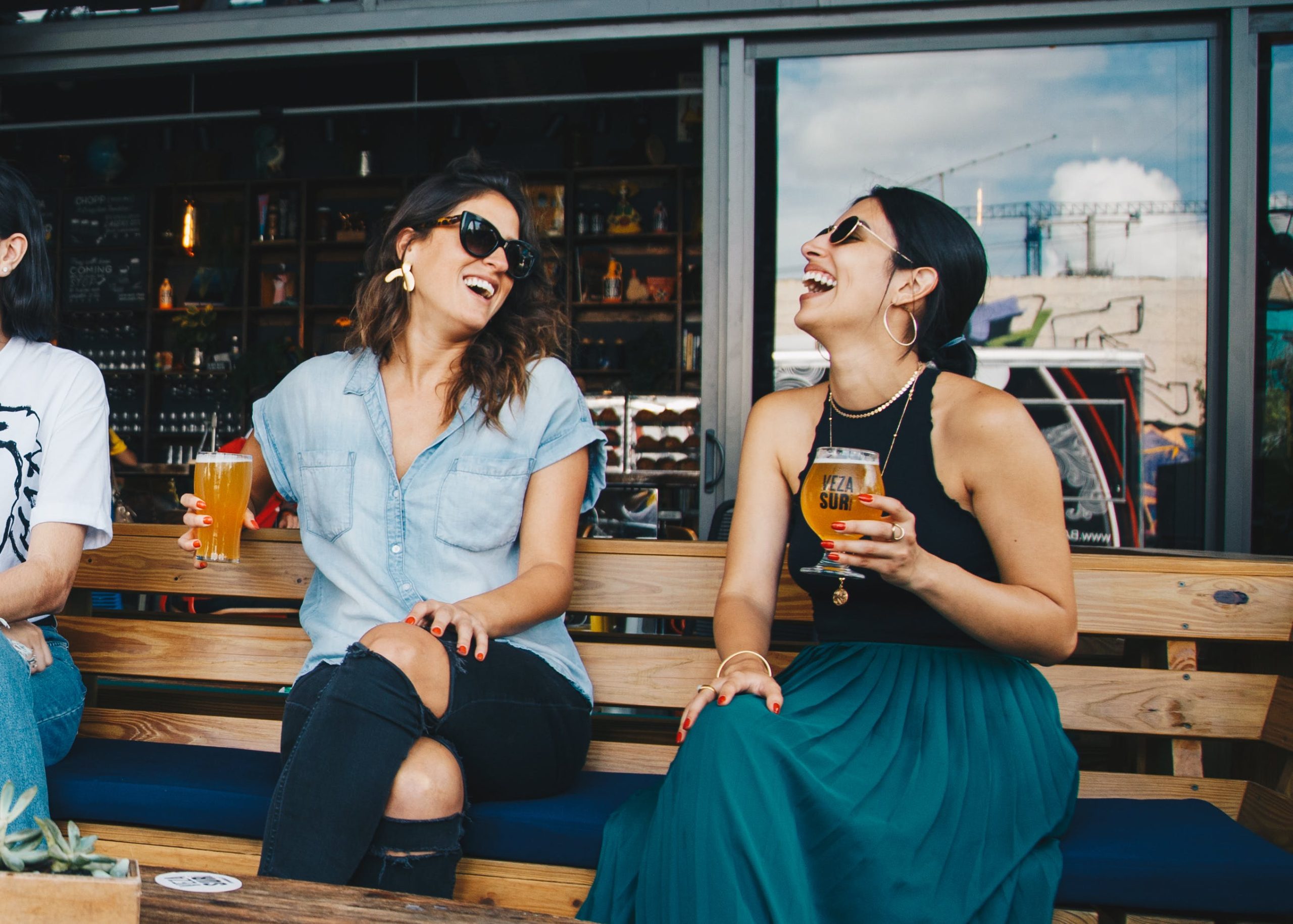 two females drinking and laughing, sitting outside.
